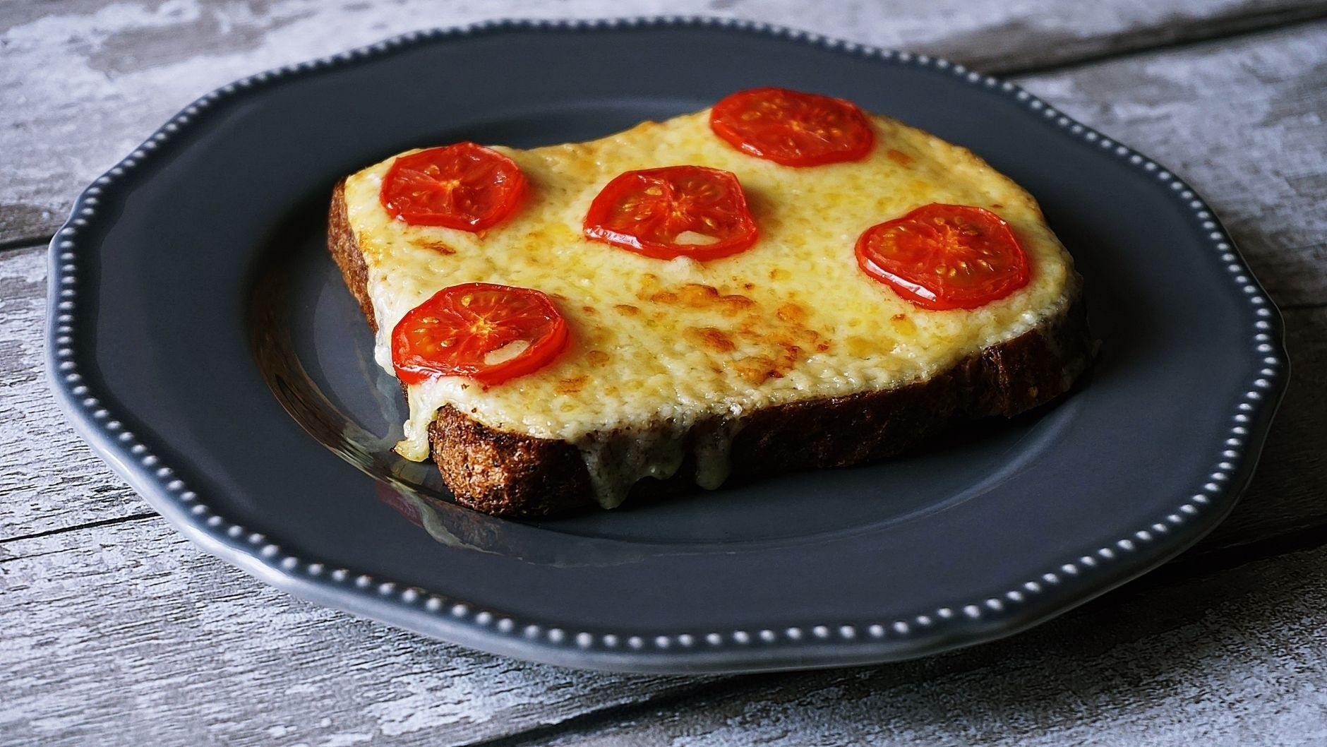 Melted cheese and tomato-topped toast on a dark plate